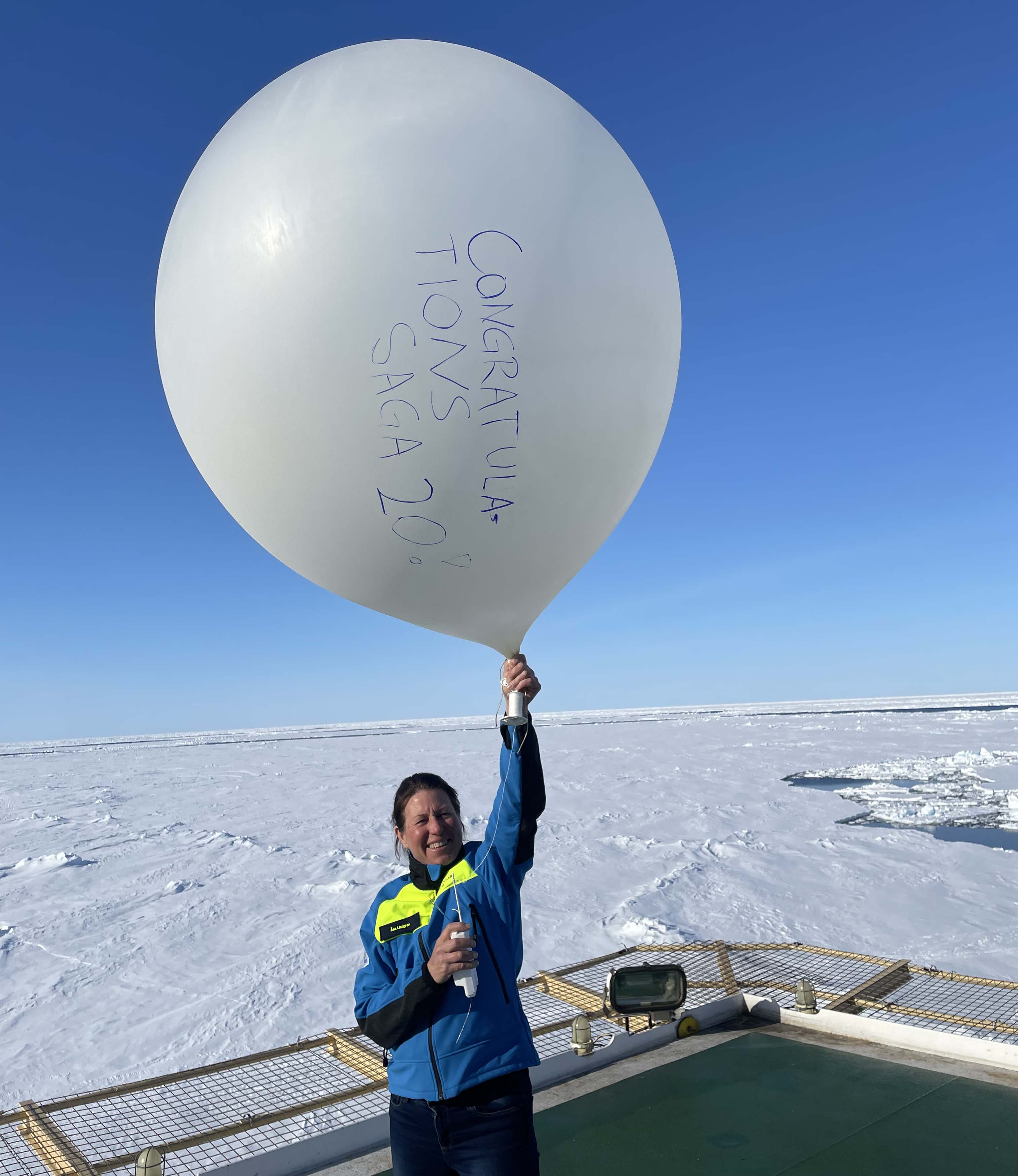 Person i blå och gul jacka som håller upp en väderballong med handskriven text