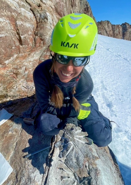 En kvinna i gul hjälm håller i ett stenprov.