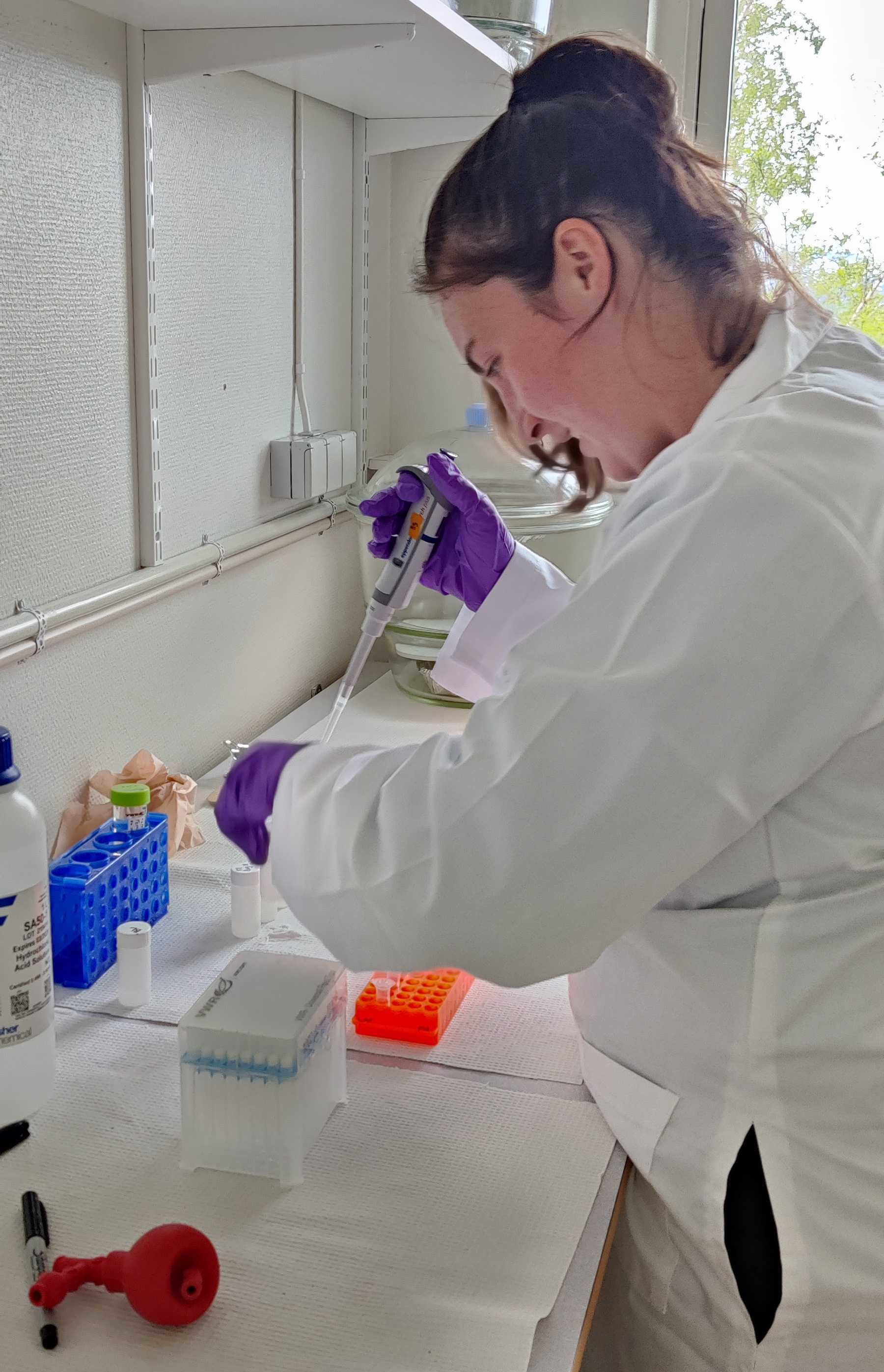 En kvinna arbetar i en vit rock i labbet. 