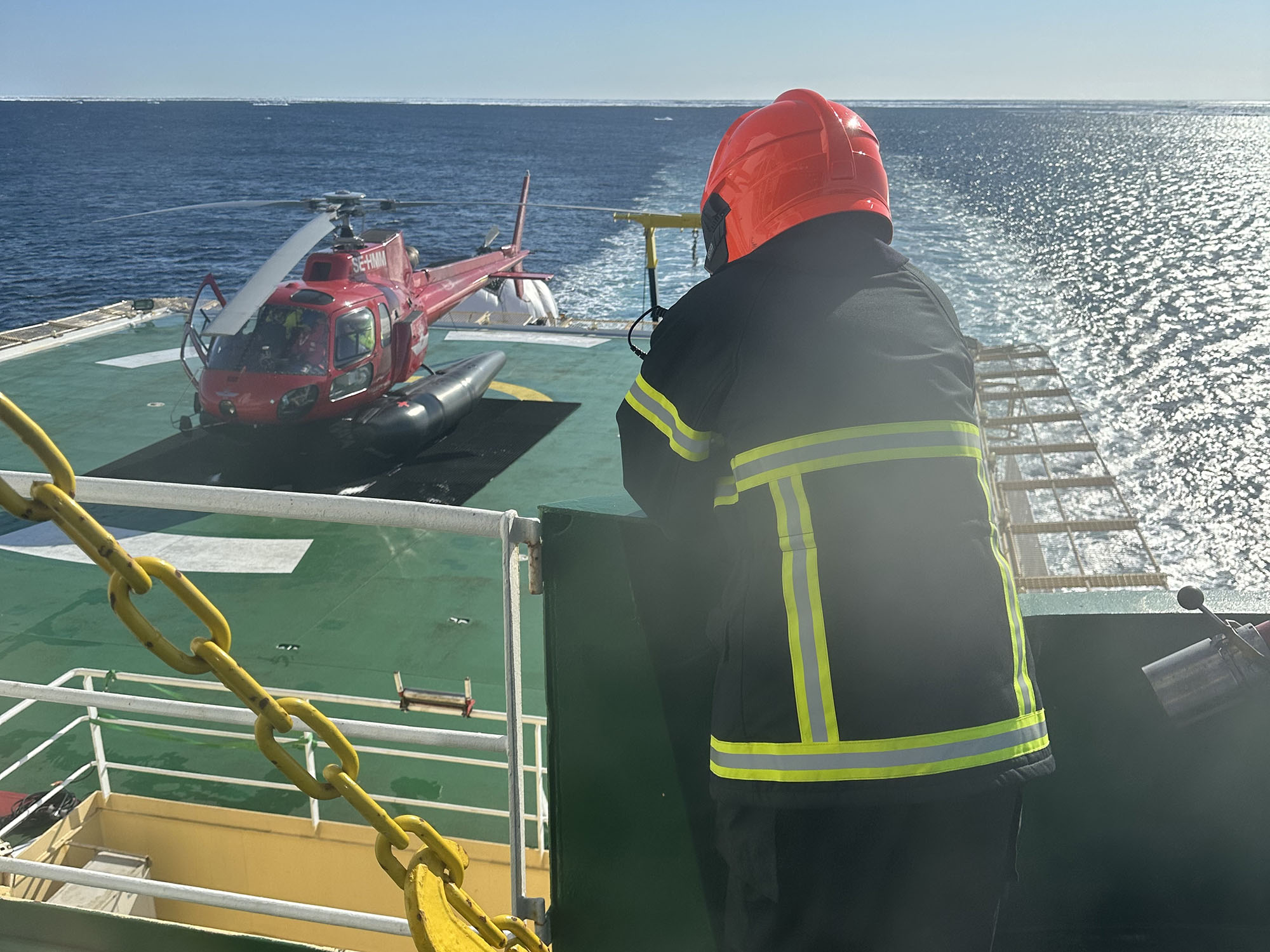 En brandman i röd hjälp står lutad mot relingen och har uppsikt över helikopterplattan. 