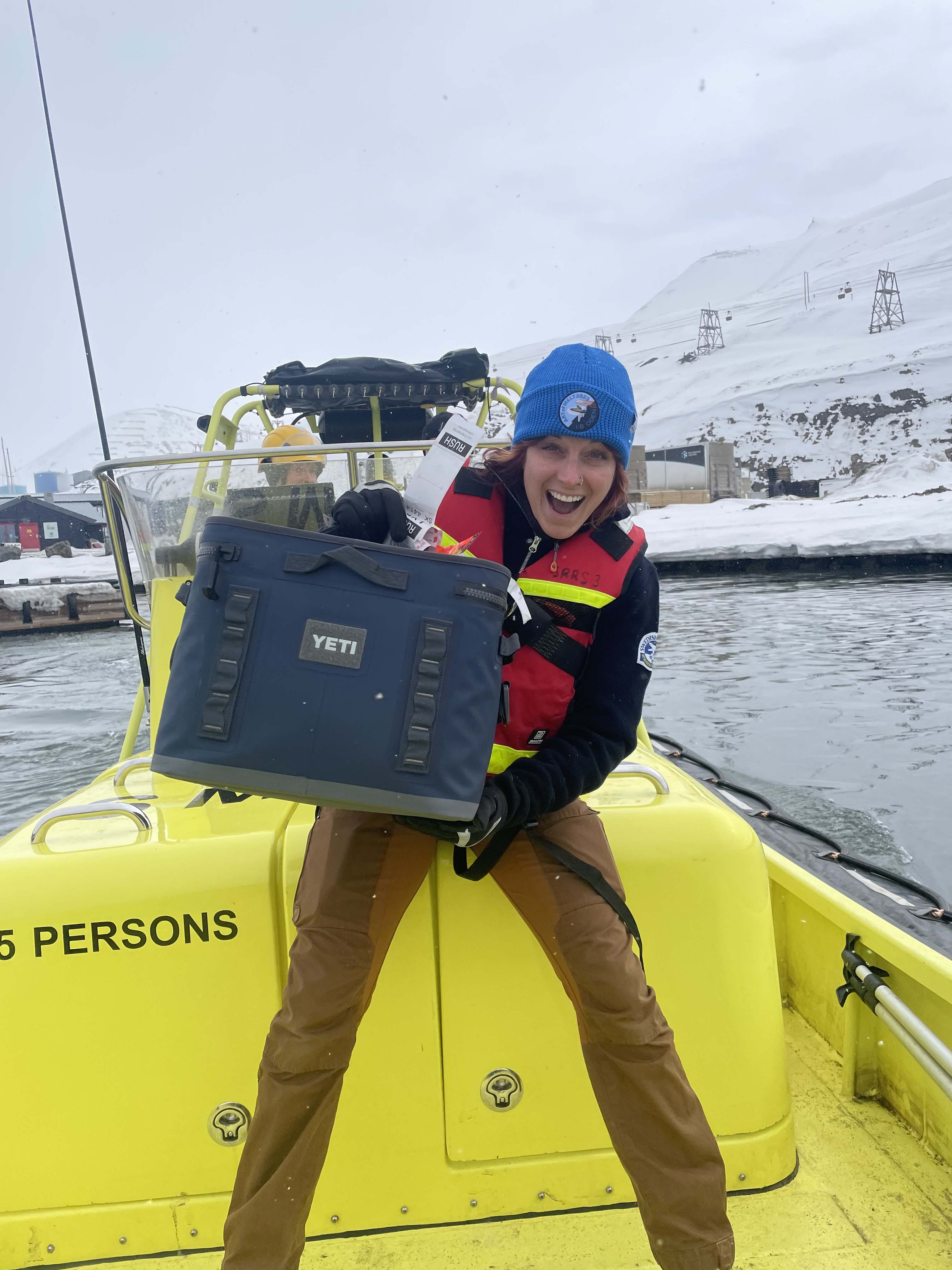 Glad kvinna står i en gul båt och håller i en blå väska.