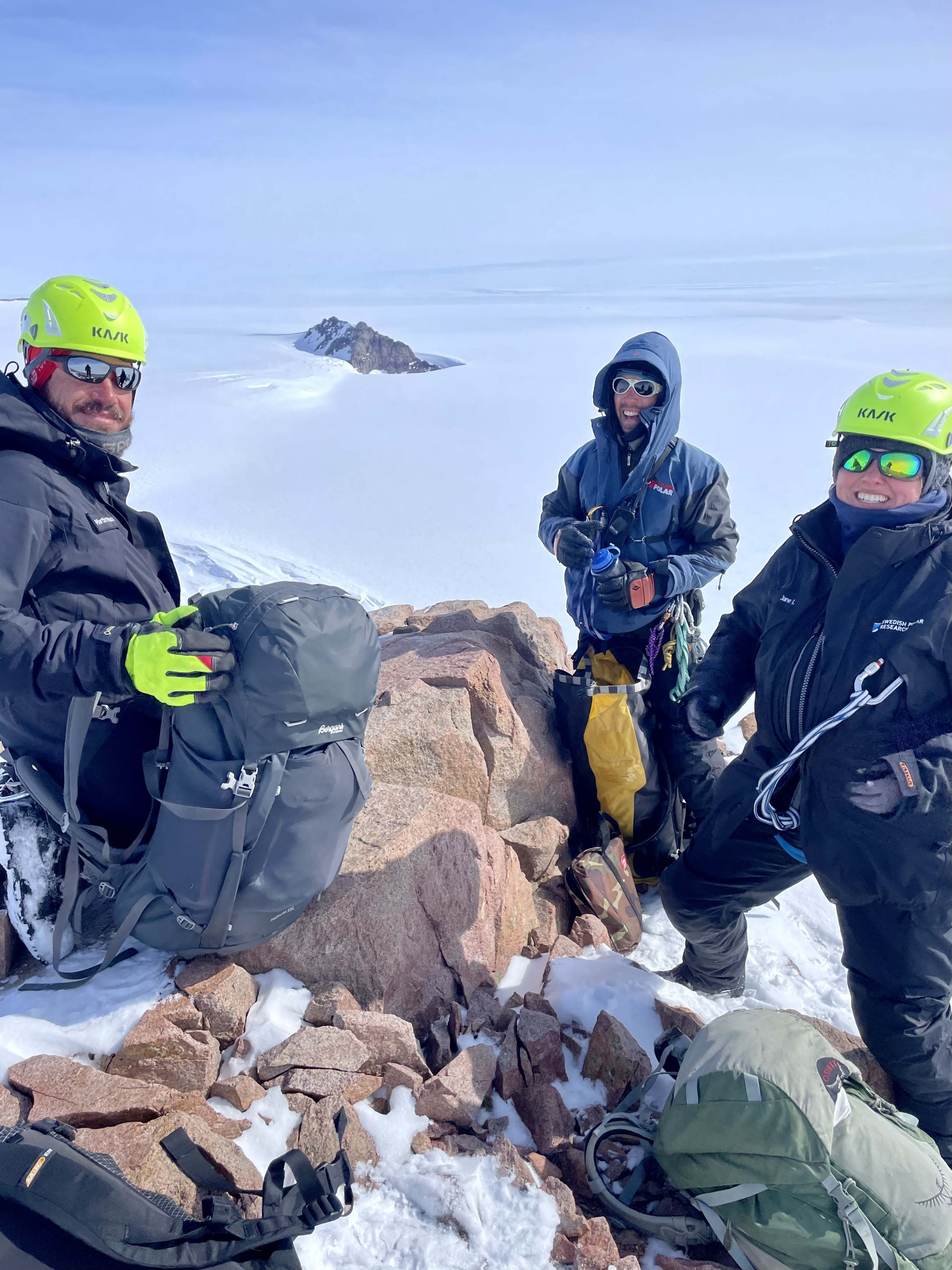 Tre personer står uppe på en klippa och ler mot kameran. 
