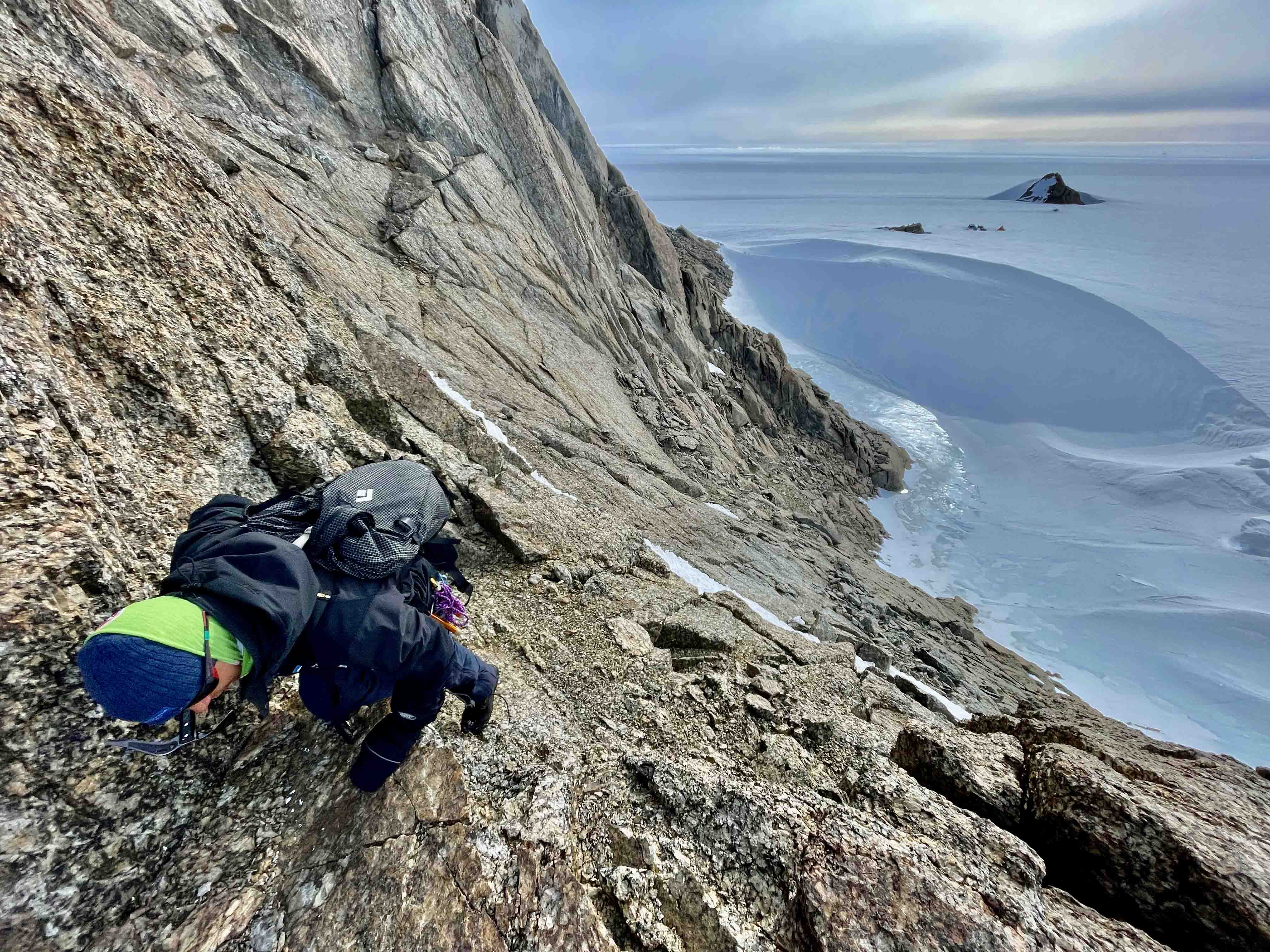 Person som klättrar på en bergsrygg. I bakgrunden syns milsvida glaciärer. 